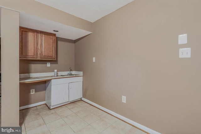 kitchen with baseboards, light countertops, a sink, brown cabinets, and light tile patterned flooring
