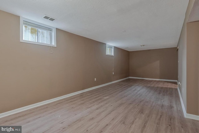 below grade area with light wood-style flooring, a textured ceiling, and baseboards