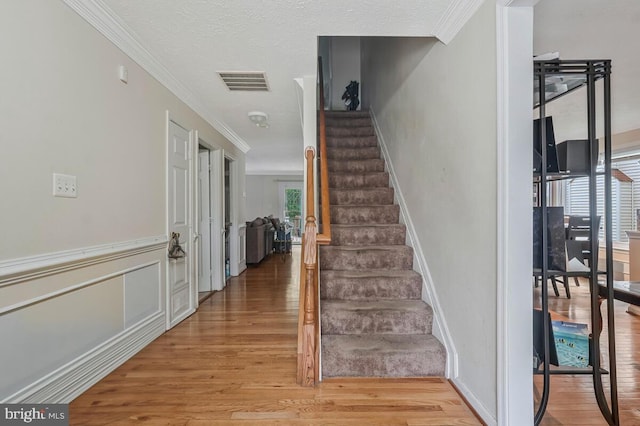 staircase featuring wood finished floors, crown molding, and baseboards