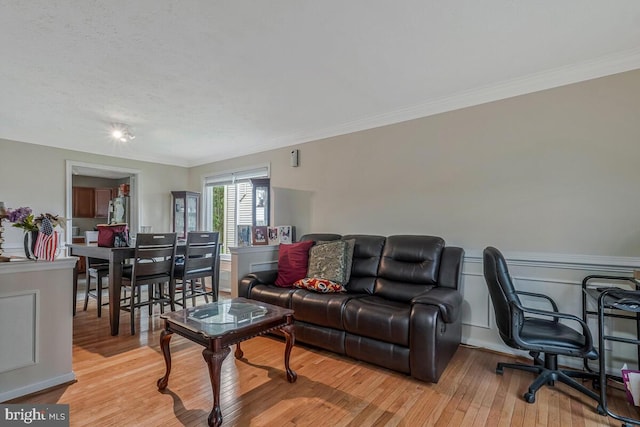 living room featuring light wood-style floors, crown molding, and wainscoting