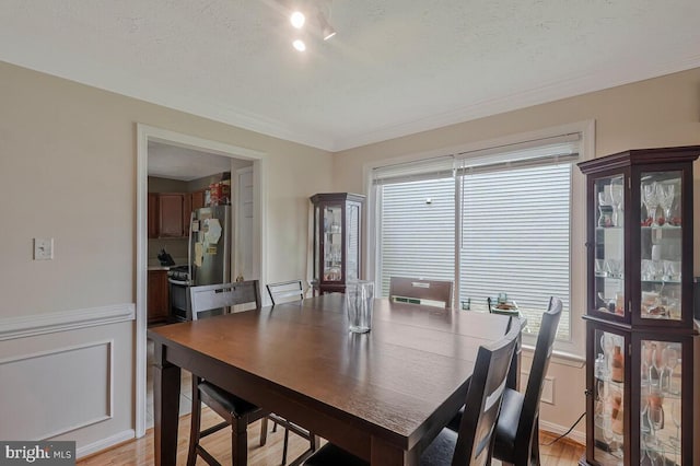 dining space featuring light wood-style flooring, wainscoting, and a textured ceiling
