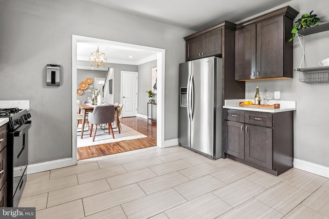 kitchen with stainless steel fridge, gas stove, light countertops, dark brown cabinets, and a chandelier