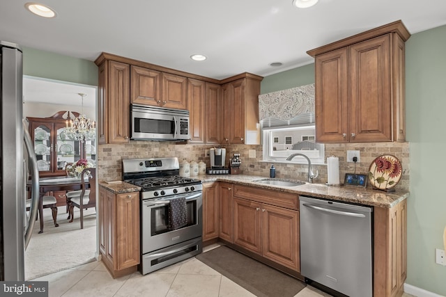 kitchen featuring appliances with stainless steel finishes, a sink, stone counters, brown cabinetry, and tasteful backsplash