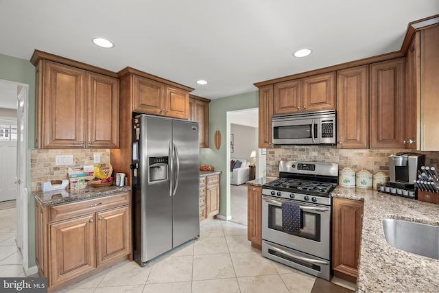 kitchen with stainless steel appliances, light stone counters, tasteful backsplash, brown cabinets, and light tile patterned floors