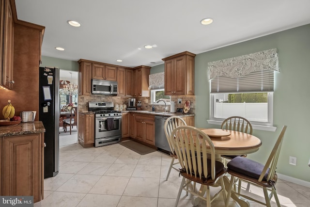 kitchen featuring appliances with stainless steel finishes, a sink, backsplash, brown cabinets, and recessed lighting