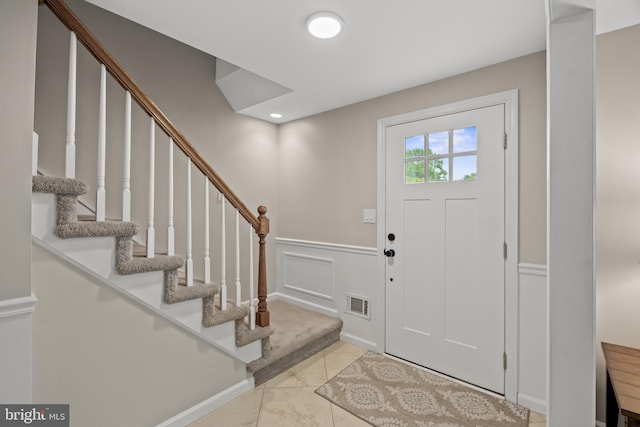 foyer entrance featuring a wainscoted wall, stairway, a decorative wall, and light marble finish floors