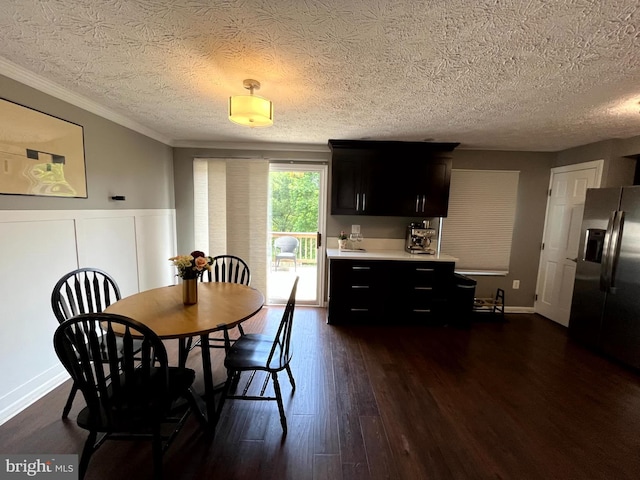 dining area featuring dark wood-style flooring, a textured ceiling, wainscoting, and crown molding
