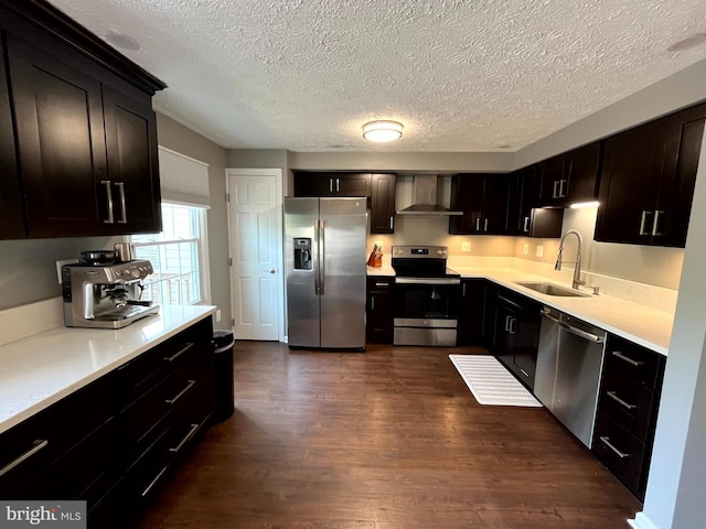 kitchen with appliances with stainless steel finishes, a sink, wall chimney exhaust hood, dark wood-style floors, and light countertops