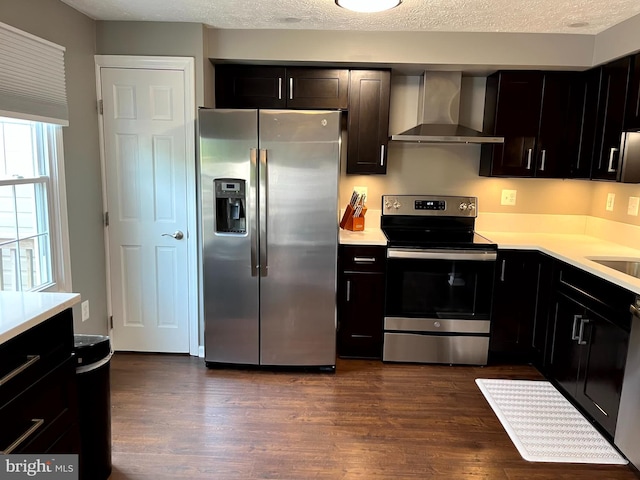 kitchen with stainless steel appliances, wall chimney range hood, light countertops, dark wood-style floors, and a textured ceiling