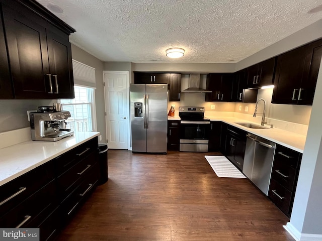 kitchen with stainless steel appliances, wall chimney range hood, dark wood-style floors, a textured ceiling, and a sink
