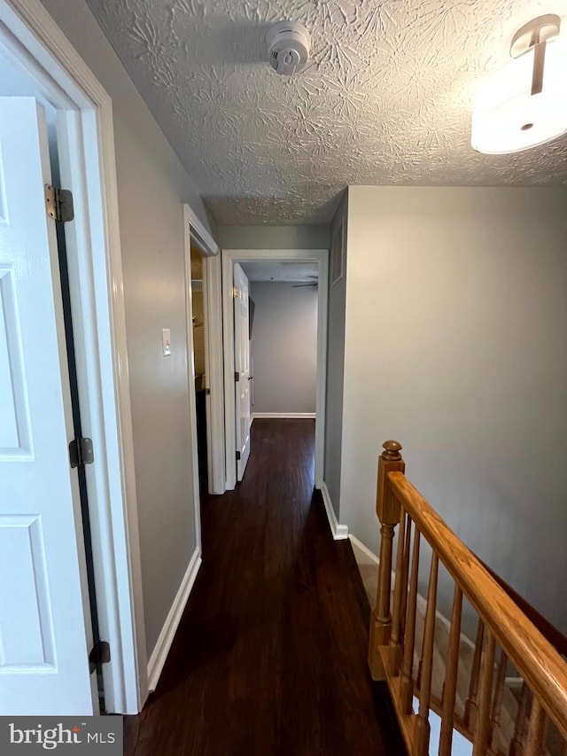 corridor featuring baseboards, wood finished floors, and an upstairs landing
