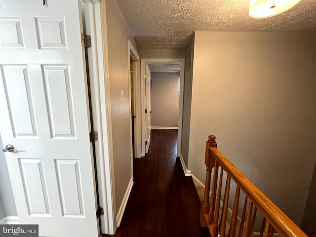 corridor featuring an upstairs landing, wood finished floors, baseboards, and a textured ceiling