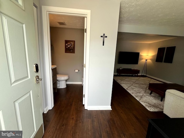 corridor featuring wood finished floors, baseboards, and a textured ceiling
