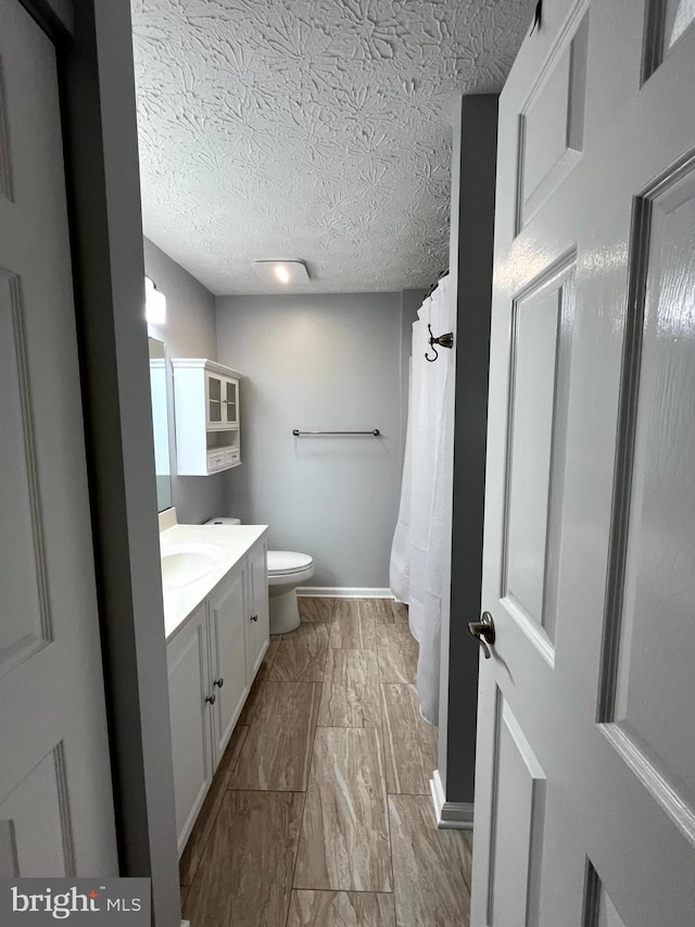bathroom with toilet, vanity, baseboards, and a textured ceiling