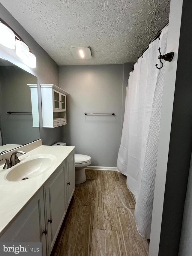 bathroom with vanity, toilet, wood finished floors, a textured ceiling, and baseboards