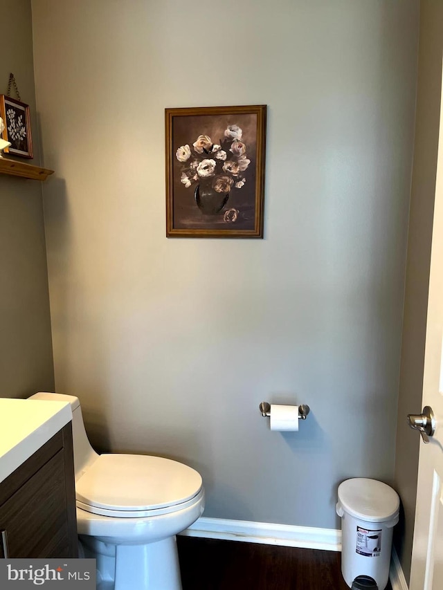 half bath featuring baseboards, toilet, wood finished floors, and vanity