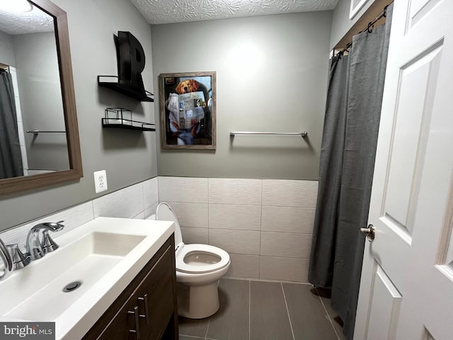 full bathroom with tile walls, toilet, tile patterned flooring, vanity, and wainscoting