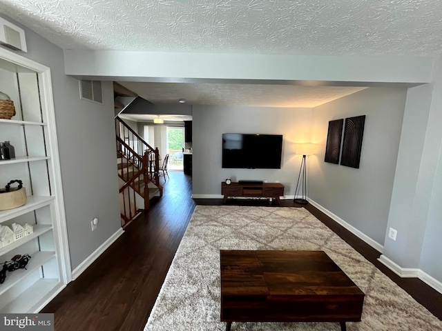 living area featuring a textured ceiling, stairway, dark wood-type flooring, and baseboards