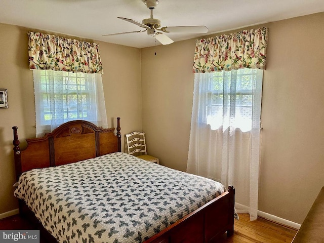 bedroom with multiple windows, wood finished floors, baseboards, and a ceiling fan