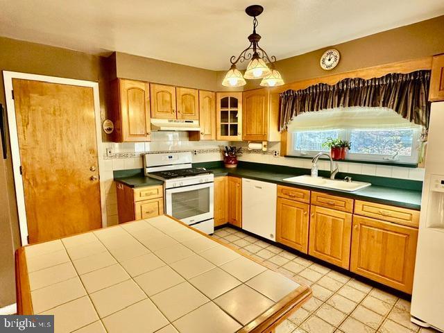 kitchen with white appliances, under cabinet range hood, a sink, decorative backsplash, and pendant lighting