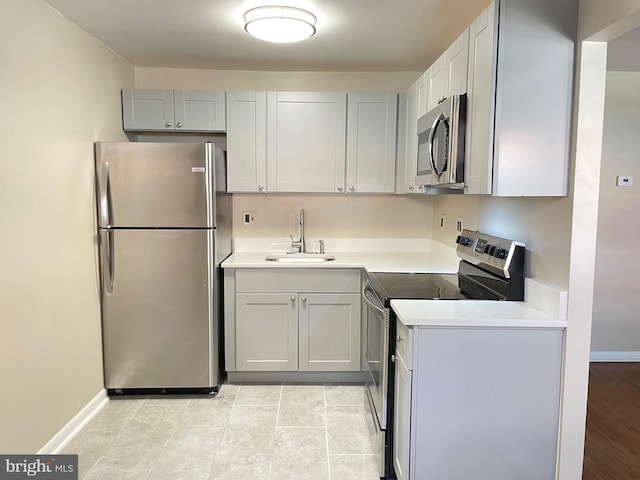 kitchen with appliances with stainless steel finishes, a sink, light countertops, and baseboards