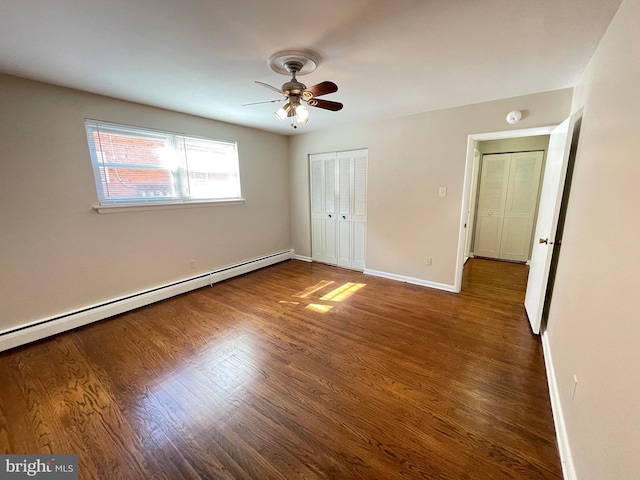 unfurnished bedroom with baseboard heating, wood finished floors, a closet, and baseboards