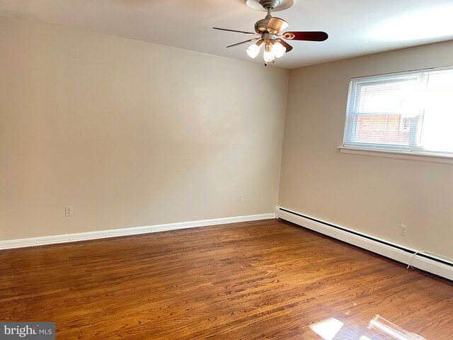 empty room featuring baseboard heating, wood finished floors, a ceiling fan, and baseboards