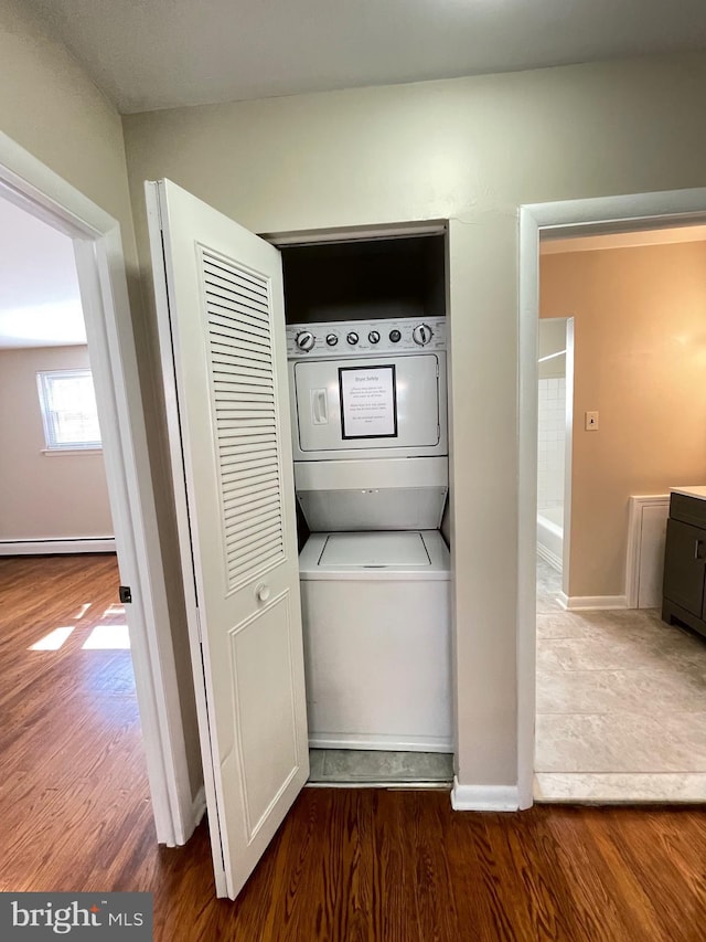 washroom featuring stacked washing machine and dryer, wood finished floors, baseboards, and a baseboard radiator
