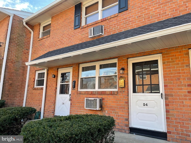 view of exterior entry featuring brick siding and an AC wall unit