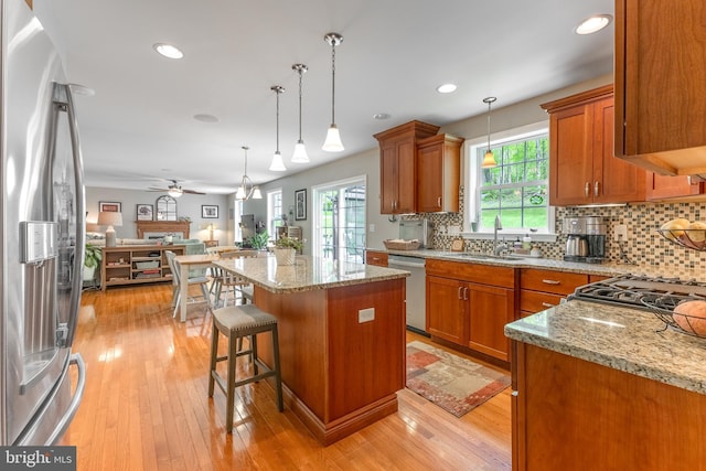 kitchen featuring appliances with stainless steel finishes, a sink, open floor plan, brown cabinets, and backsplash