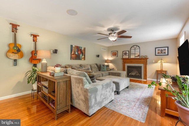 living area with ceiling fan, light wood-style flooring, baseboards, and a fireplace with flush hearth