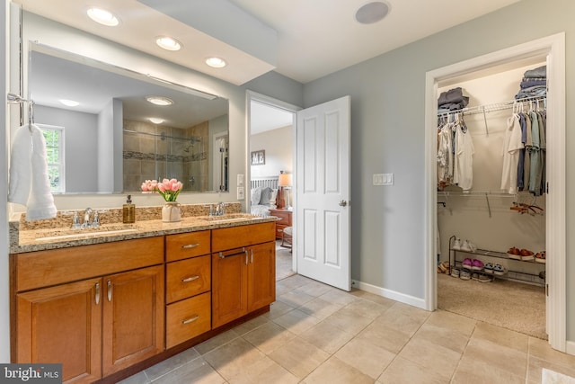 bathroom with a shower stall, double vanity, a spacious closet, baseboards, and tile patterned floors