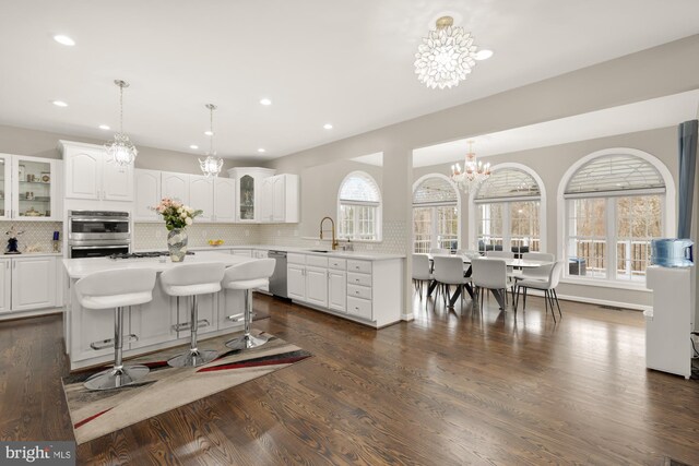 kitchen with a chandelier, light countertops, glass insert cabinets, stainless steel appliances, and backsplash