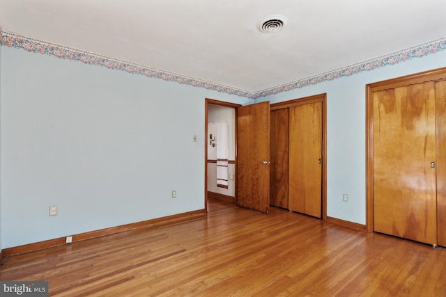 unfurnished bedroom featuring multiple closets, light wood finished floors, and baseboards