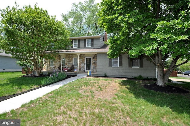 traditional-style house with a front yard, a chimney, a porch, and stone siding