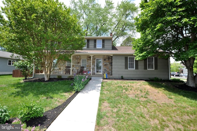 traditional-style home with covered porch, a front yard, a chimney, and stone siding