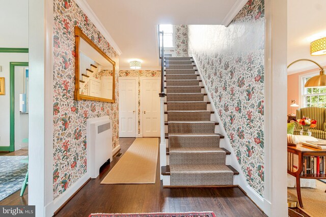 stairway with wallpapered walls, wood finished floors, baseboards, crown molding, and radiator