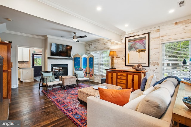 living room featuring dark wood finished floors, a glass covered fireplace, a ceiling fan, recessed lighting, and crown molding