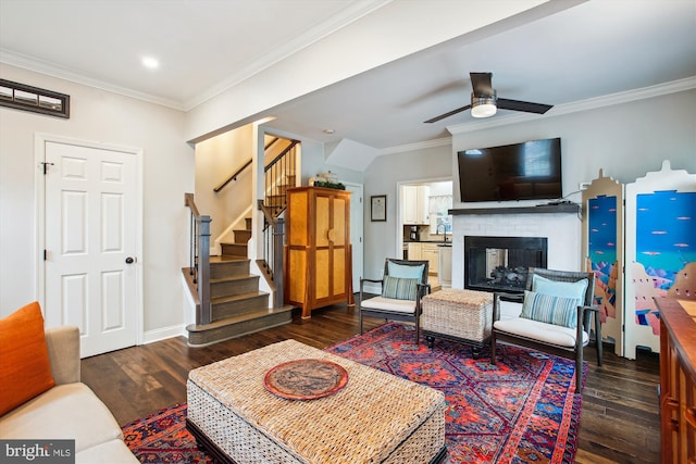 living area featuring wood finished floors, stairs, crown molding, a ceiling fan, and a fireplace
