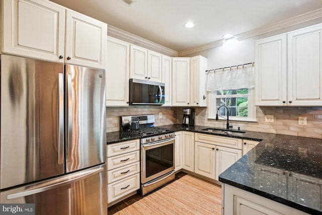 kitchen with stainless steel appliances, a sink, crown molding, dark stone countertops, and light wood-style flooring