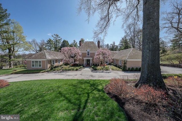 view of front of property featuring a chimney, stucco siding, a front lawn, and curved driveway