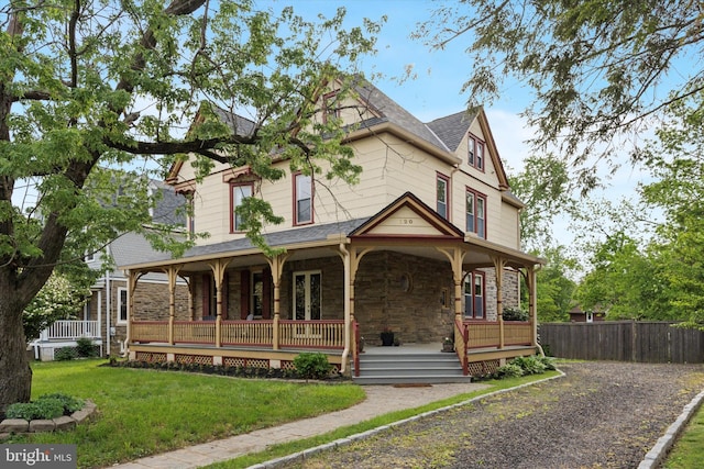 victorian home featuring stone siding, covered porch, and roof with shingles