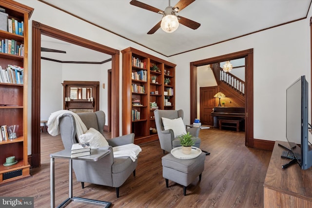 living area with a ceiling fan, wood finished floors, crown molding, and baseboards