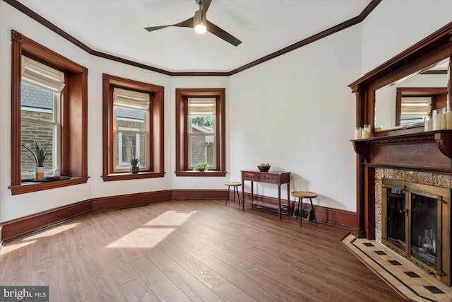 sitting room with a premium fireplace, ceiling fan, wood finished floors, ornamental molding, and baseboards