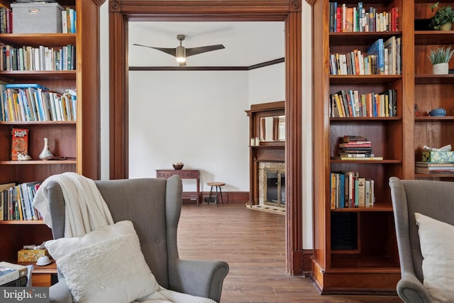 living area with a fireplace, a ceiling fan, wood finished floors, ornamental molding, and baseboards