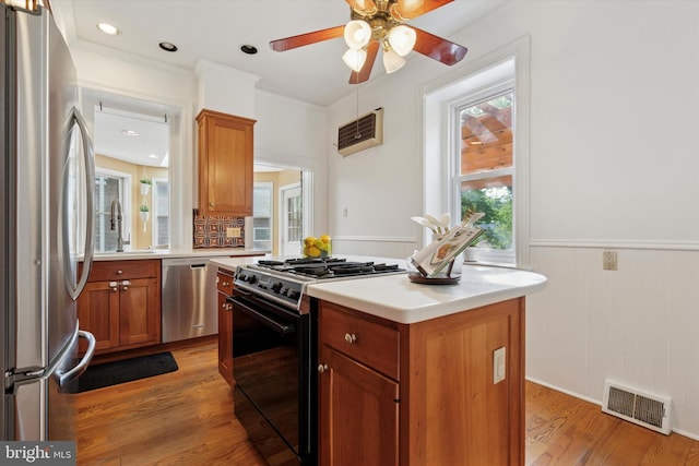 kitchen featuring stainless steel appliances, ceiling fan, a sink, wainscoting, and light wood-type flooring
