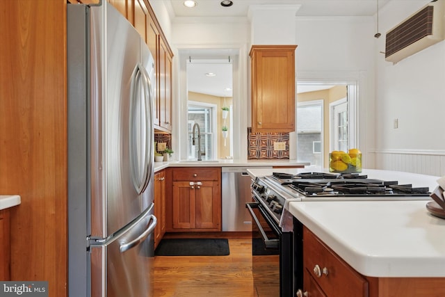 kitchen with appliances with stainless steel finishes, a sink, light wood finished floors, brown cabinets, and crown molding