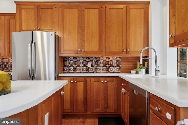 kitchen featuring appliances with stainless steel finishes, a sink, brown cabinetry, light countertops, and decorative backsplash