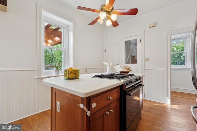 kitchen with black gas range oven, a wainscoted wall, healthy amount of natural light, light wood finished floors, and a ceiling fan
