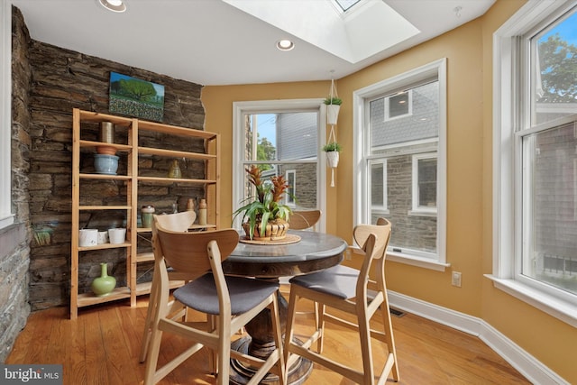 dining area with a skylight, light wood-type flooring, recessed lighting, and baseboards